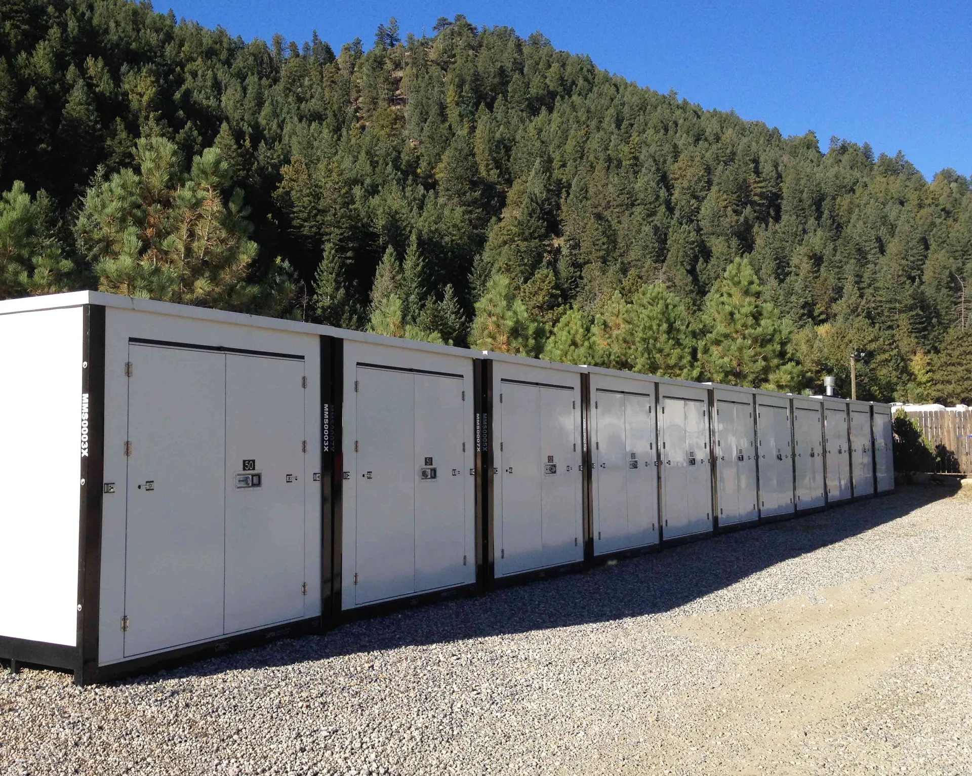 White storage containers on gravel beside a wooded hillside
